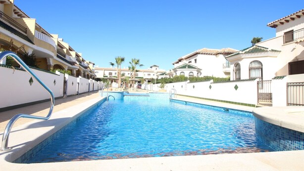A swimming pool surrounded by multi-story buildings with balconies, a clear blue sky, and palm trees. - Family house Cuidad Quesada  Rojales (Ciudad Quesada)