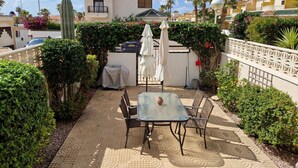 A patio with a table and chairs, surrounded by greenery and a building with a tiled roof. - Family house Cuidad Quesada  Rojales (Ciudad Quesada)