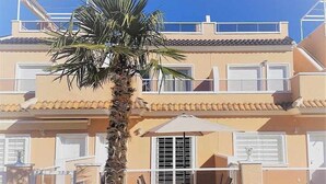 Ein mehrstöckiges Gebäude mit Balkonen, einer Palme und einer Terrasse mit Gartenmöbeln.