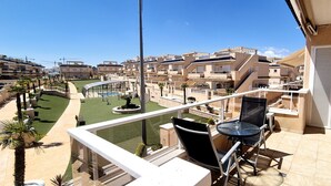 En balkon med udsigt over en swimmingpool, palmer og anlagt område.