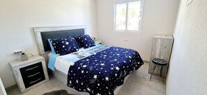 Una camera da letto con un letto, un comodino, un piccolo armadio, una finestra e una sedia.
