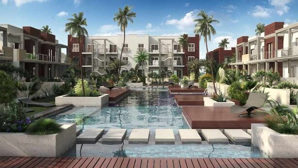 A modern hotel with a central pool, surrounded by lush greenery and palm trees.