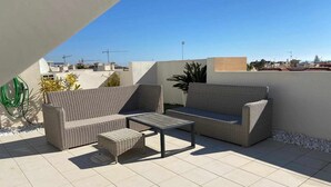 An outdoor patio area with a wicker sofa, a small table, and a garden hose.