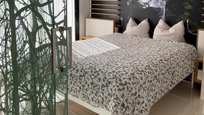 A modern bedroom with a large bed, a glass partition, a wall-mounted shelf, and a large nature-themed mural.