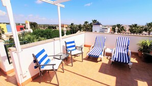 A rooftop terrace with two striped lounge chairs, a small table, and a potted plant.