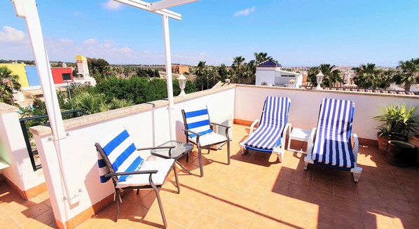 A rooftop terrace with two striped lounge chairs, a small table, and a potted plant.