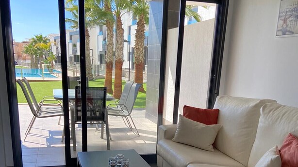 Una sala moderna con un sofá, una mesa de centro y vistas a una piscina y palmeras a través de amplias puertas de cristal.