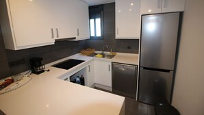 Una cocina moderna con armarios blancos, un refrigerador de acero inoxidable, lavavajillas y cafetera.