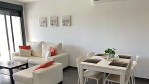Una sala moderna con un sofá, una mesa de centro y una mesa de comedor con sillas. Hay tres obras de arte enmarcadas en la pared.
