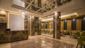 Un vestíbulo de hotel con mostrador de recepción, bar de aperitivos y zona de restaurante.