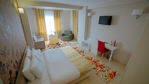 Una habitación de hotel con cama, escritorio, silla, televisión y ventana con cortinas.