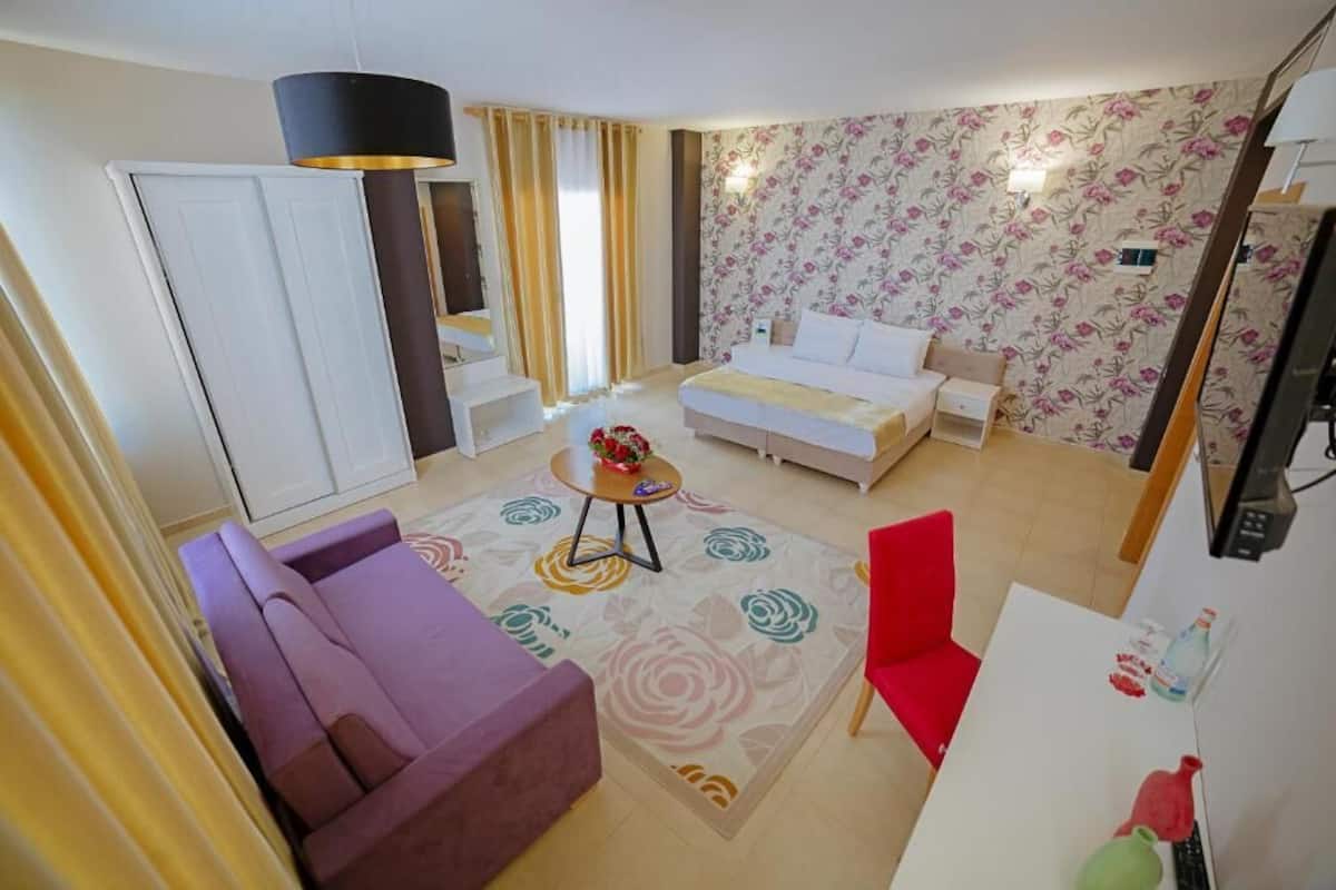 Une chambre d’hôtel avec un lit, un canapé, un fauteuil rouge, une petite table avec un vase et une armoire.