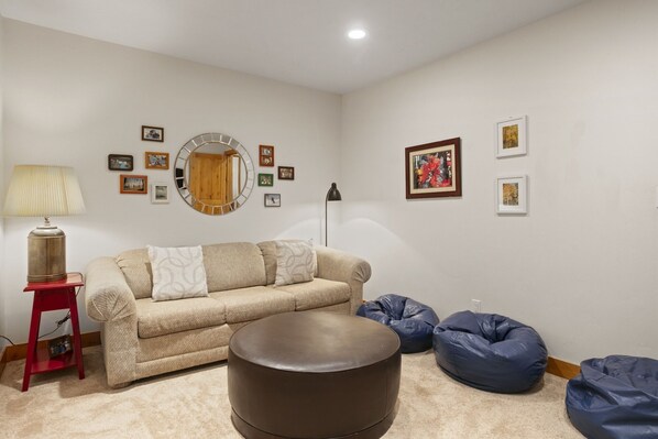A living room with a beige sofa, a round ottoman, and blue bean bags. - Mountain and Forest Views | Fireplace (Park City)