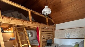 A cozy loft-style room with a wooden ceiling, a loft bed, a TV, a sofa, and a patterned rug. - Casa Edera  (Locarno)