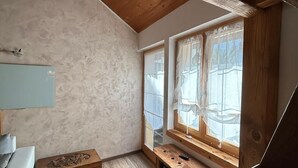A compact room with a sloped ceiling, a wooden desk, a white sofa, and a window with sheer curtains. - Casa Edera  (Locarno)