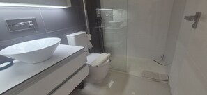 A bathroom with a large white sink, a toilet, and a glass shower enclosure.
