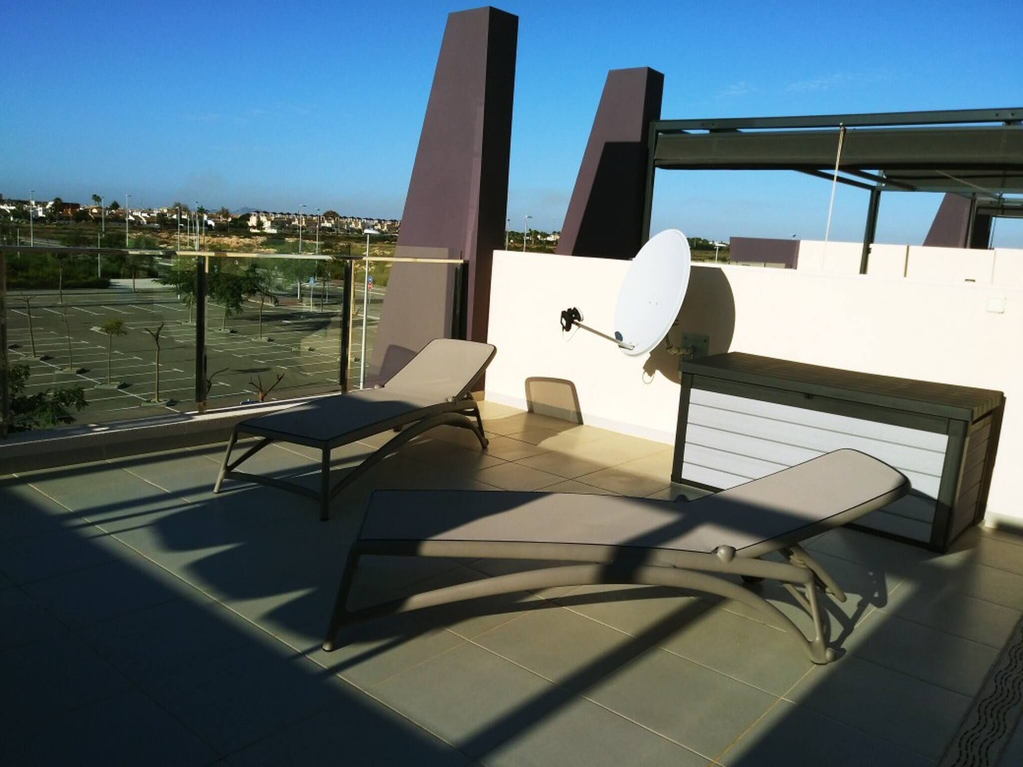 A rooftop terrace with two lounge chairs, a table, and a satellite dish.