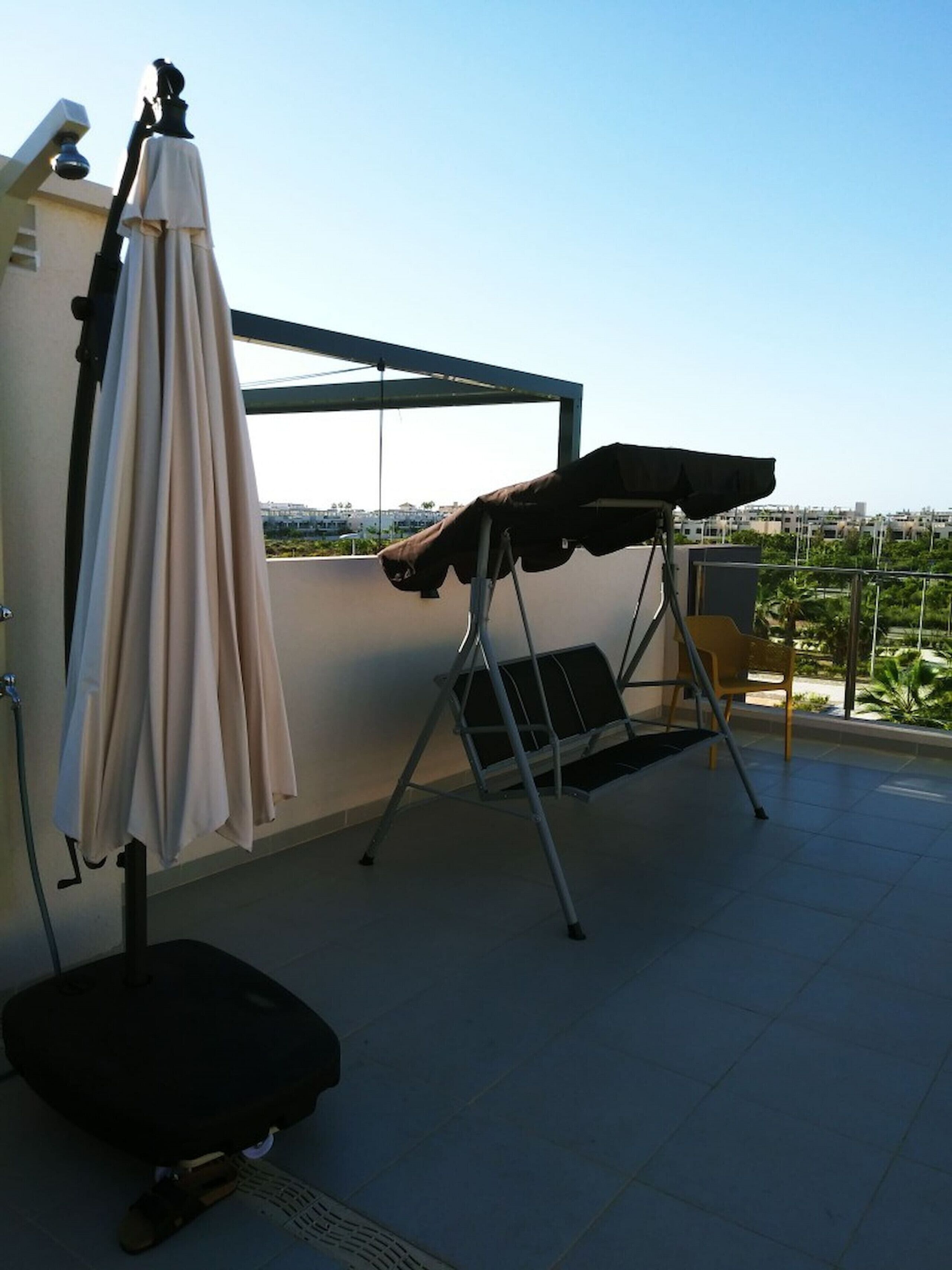 Una terraza en la azotea con una parrilla cubierta, una silla plegable y una sombrilla.