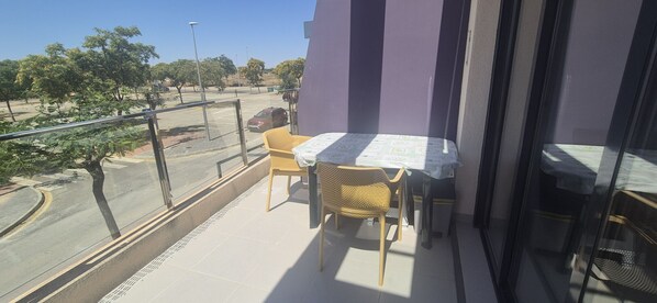 A balcony with a table and chairs, a view of a road and trees, and a purple wall.