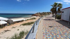 A beachside walkway with a tiled path, palm trees, and a view of the ocean. - Penthouse Elisa Mil Palmeras (Torre de la Horadada)