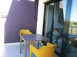 A balcony with a table and two chairs, a sliding glass door, and a view of the cityscape.