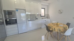A modern kitchen with built-in appliances, a dining area with a round table, and a large window. - Penthouse Elisa Mil Palmeras (Torre de la Horadada)