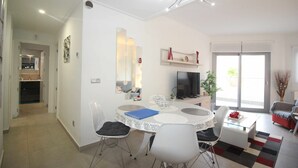 Un salon moderne avec une table à manger ronde, des chaises blanches, un téléviseur à écran plat et une grande fenêtre.