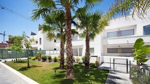 Un bâtiment moderne à la façade blanche, agrémenté de palmiers et doté d’une pelouse bien entretenue.