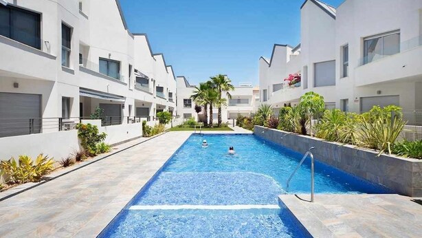 Un hôtel moderne doté d’une piscine centrale, entouré de bâtiments blancs et de palmiers.