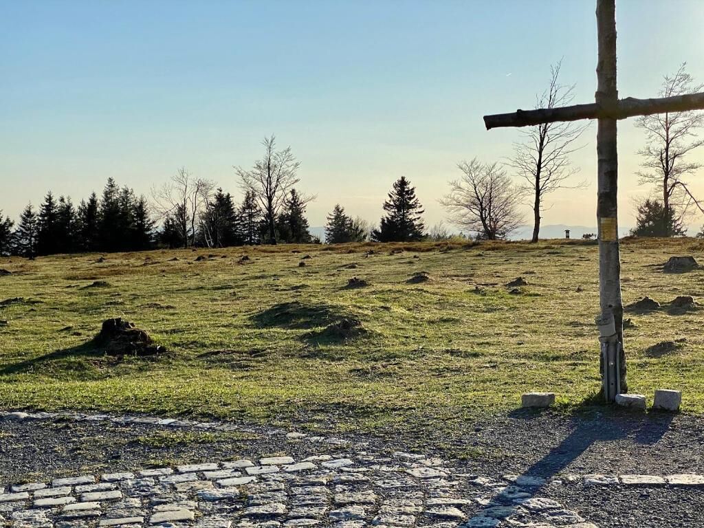 Ländliche Landschaft mit einem steinbelagten Pfad, der zu einem hölzernen Kreuz führt.