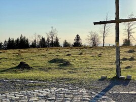 Ländliche Landschaft mit einem steinbelagten Pfad, der zu einem hölzernen Kreuz führt.