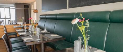 A restaurant with green leather booths and tables set with white napkins, silverware, and clear glass vases with flowers.