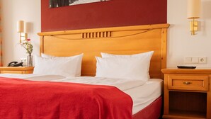 A hotel room with a large bed, a wooden headboard, a nightstand with a lamp, and a window with curtains.
