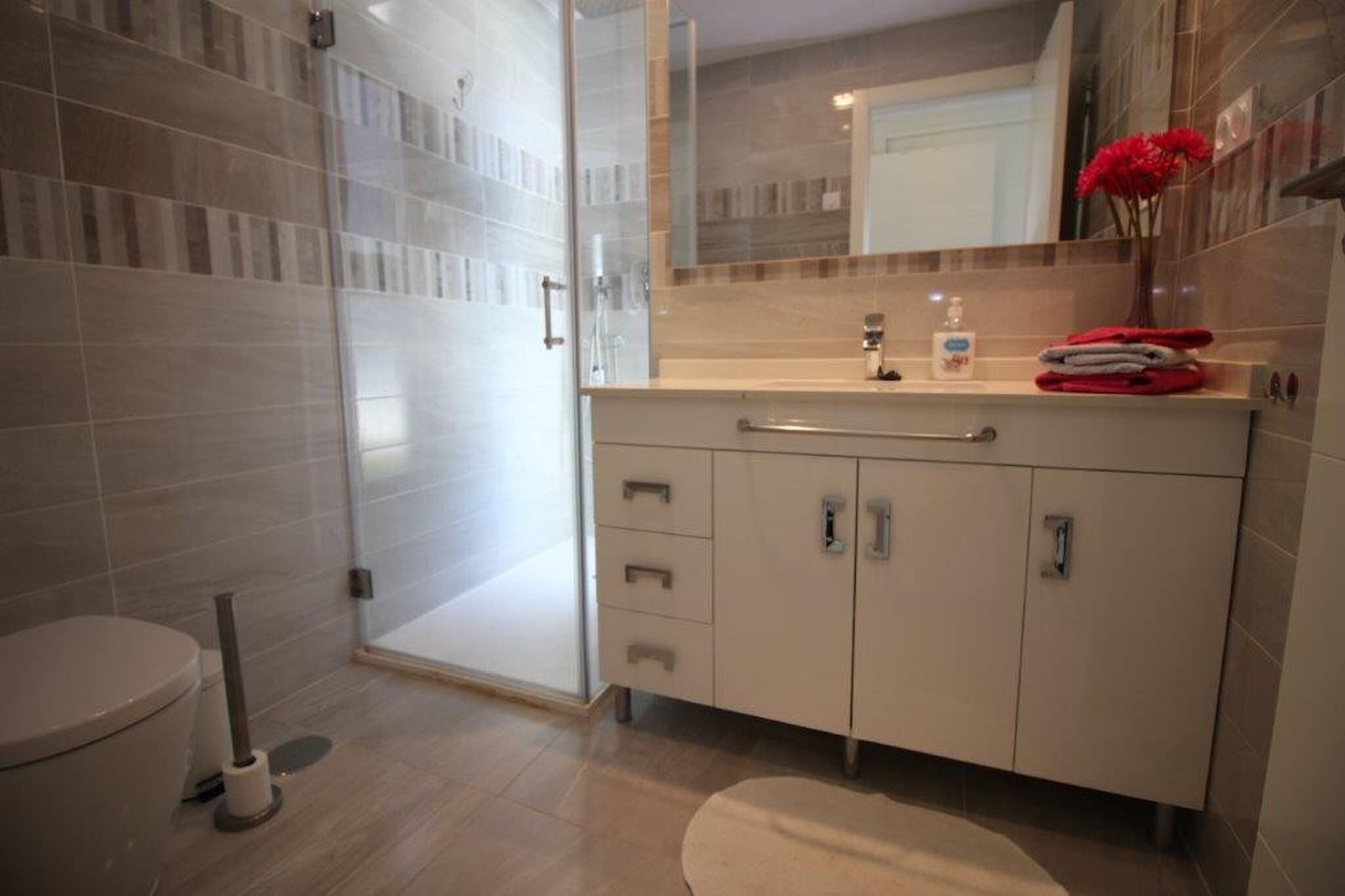 A modern bathroom with a glass shower enclosure, a white sink with a mirror, and a toilet.