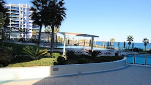 A hotel pool area with a clear view of the sea, palm trees, and a modern building in the background. - Groundfloor Sea Senses Punta Prima , Orihuela Costa (Torrevieja)
