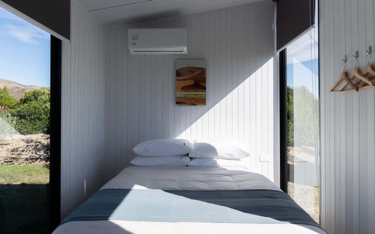 Een slaapkamer met een bed, witte muren, een schilderij en een airconditioning.