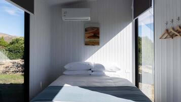 Een slaapkamer met een bed, witte muren, een schilderij en een airconditioning.