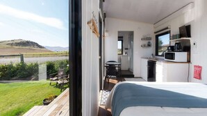 A bedroom with a bed, a small kitchenette, and a view of a grassy field. - Ruffell Ranch Cabin by Tiny Away (Tarras)