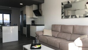 Una sala de estar moderna con un sofá, una mesa de centro con aperitivos y una cocina al fondo.