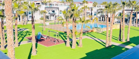 Et resort med swimmingpool, palmer og et legeområde for børn.