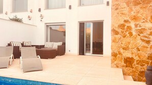 Ein Poolbereich mit Steinmauer, Sitzgelegenheiten im Freien und einer Glastür, die zu einer Terrasse führt.