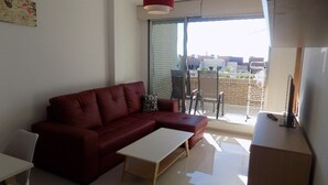 Ein modernes Wohnzimmer mit einem roten Sofa, einem weißen Couchtisch und einer Glastür zum Außenbalkon.