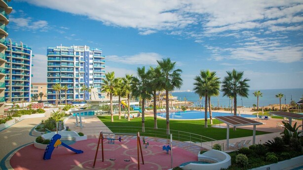 A resort with a pool, palm trees, and a playground. - Apartment Sea Senses Punta prima, Orihuela Costa (Torrevieja)