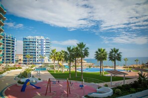A resort with a pool, palm trees, and a playground. - Apartment Sea Senses Punta prima, Orihuela Costa (Torrevieja)