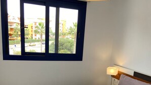 A bedroom with two beds, a window with a view of buildings and palm trees, and a bedside lamp. - Apartment Sea Senses Punta prima, Orihuela Costa (Torrevieja)