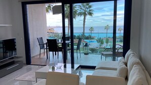 A modern living room with a large sliding glass door leading to a balcony with a view of the sea and palm trees. - Apartment Sea Senses Punta prima, Orihuela Costa (Torrevieja)