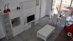 A modern living room with a flat-screen TV, white furniture, and a view of the outdoors.