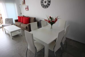 A modern living room with a white dining table, white chairs, a sofa with red cushions, and a wall clock.