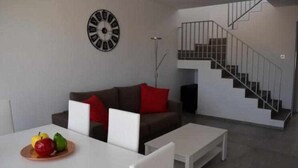 A modern living room with a staircase, a white table, and a clock on the wall.