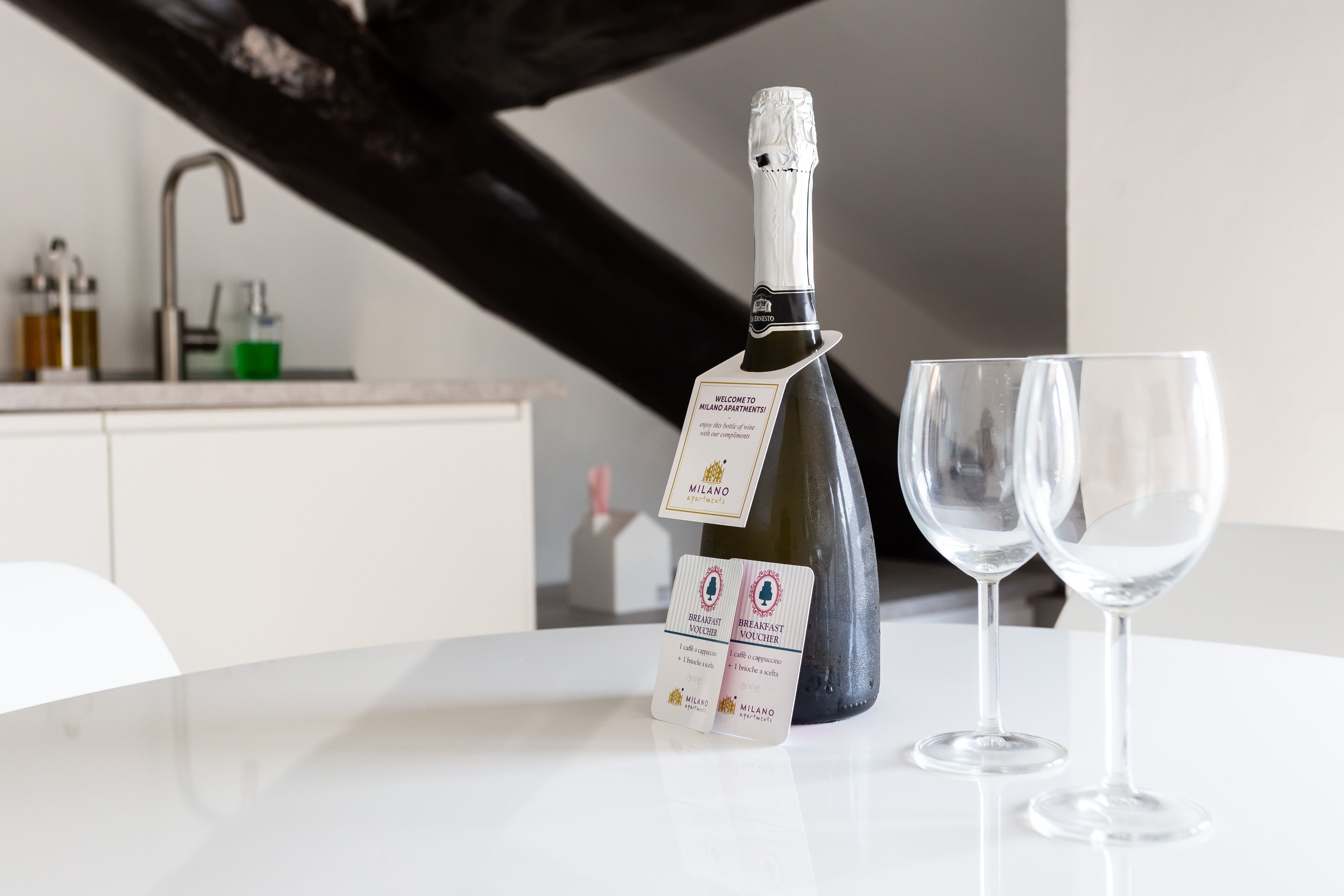 Eine Champagnerflasche und zwei Gläser auf einem weißen Tisch, im Hintergrund eine Küche.